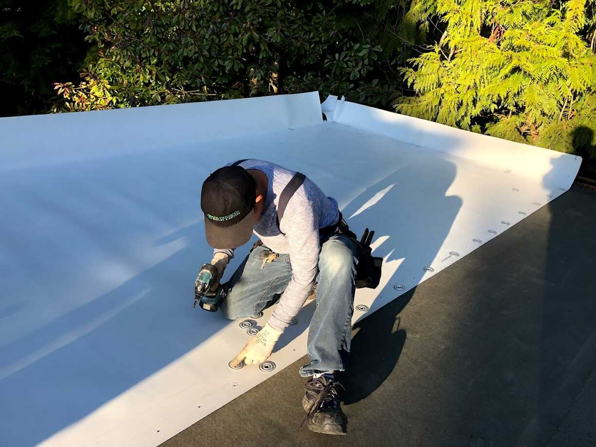 A man laying down white TPO roofing 